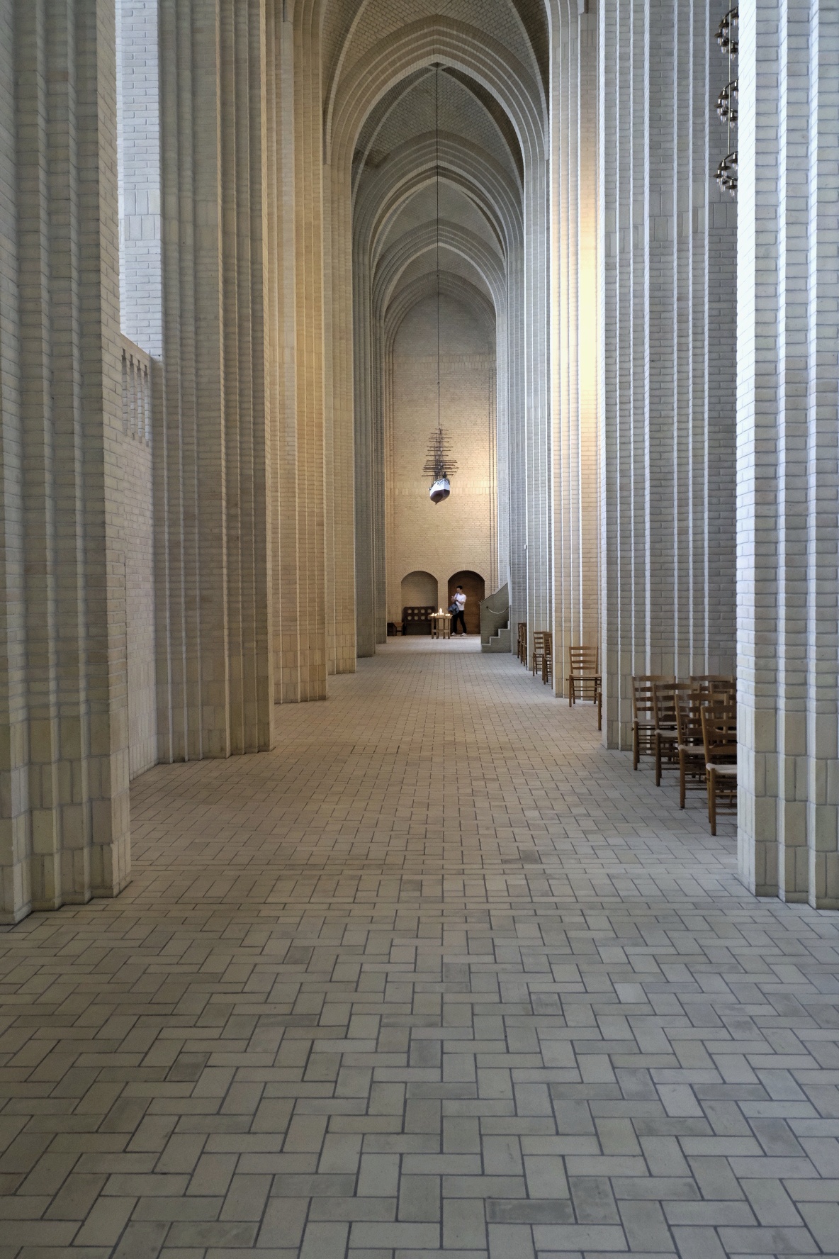 Langgestreckte Kirchen-Innenraum mit gotischen Bögen, Säulen und minimalistischer Ausstattung.