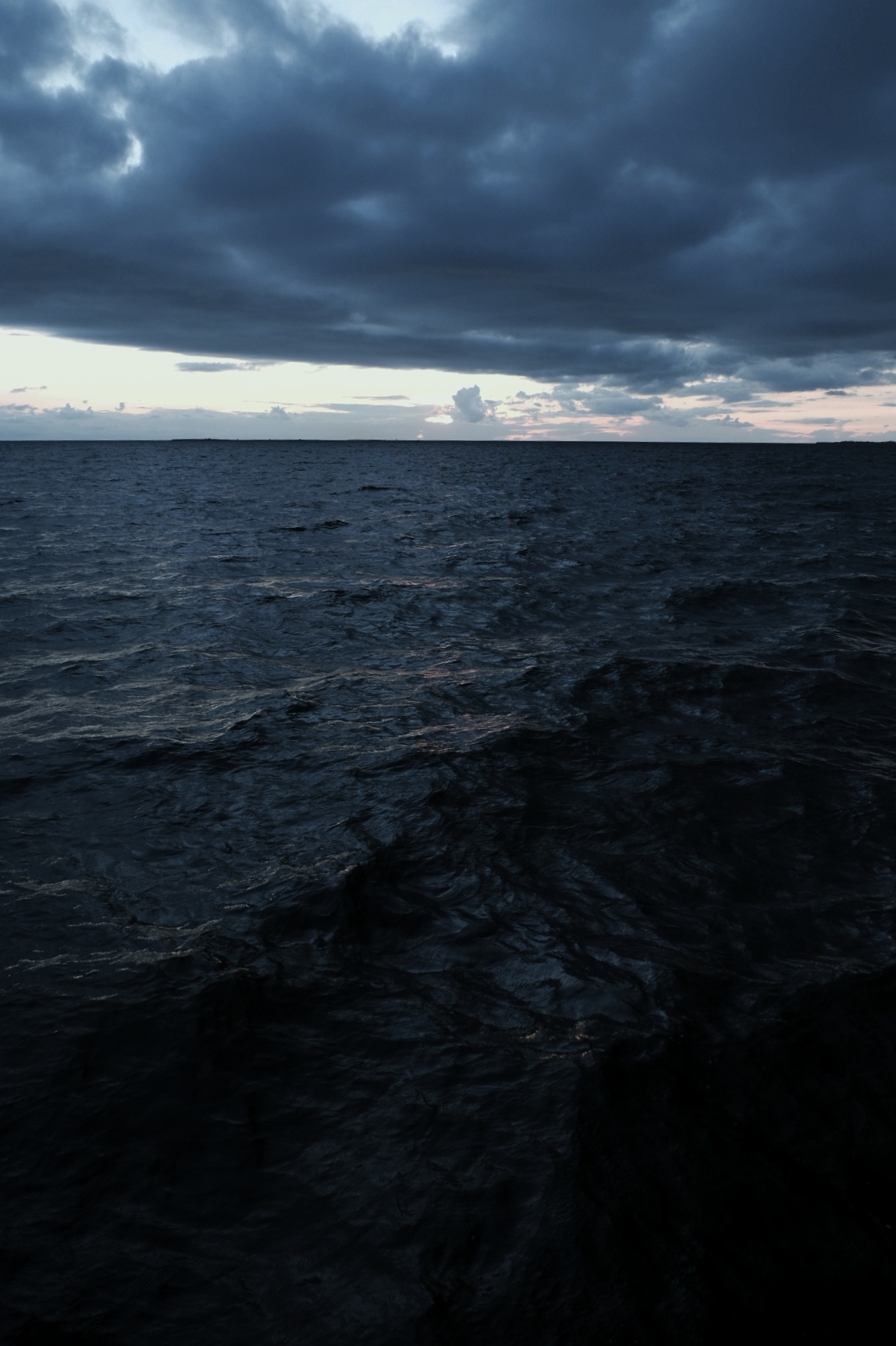 Stürmisches Meer mit dunklen Wellen und dramatischem, bewölktem Himmel bei Dämmerung.