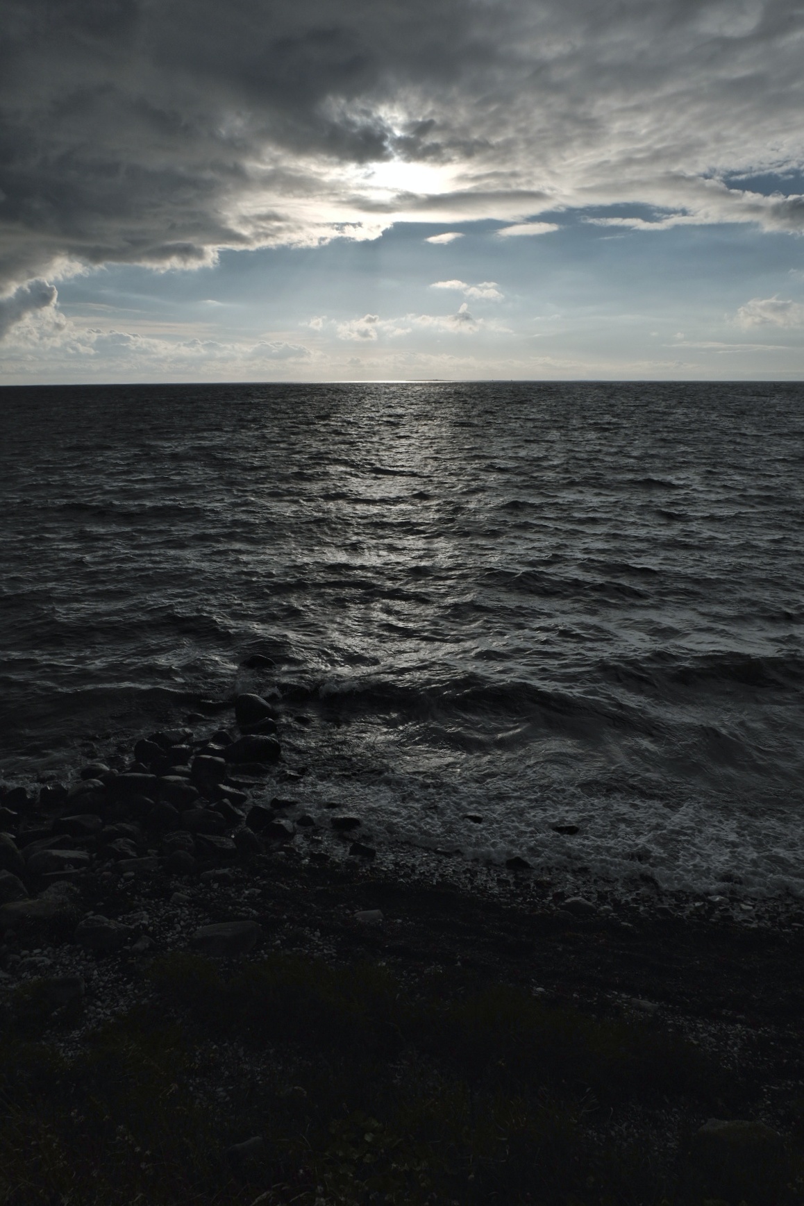 Stürmisches Meer mit dunklen Wellen, dramatischer Himmel mit Wolken und Sonnenlicht am Horizont.