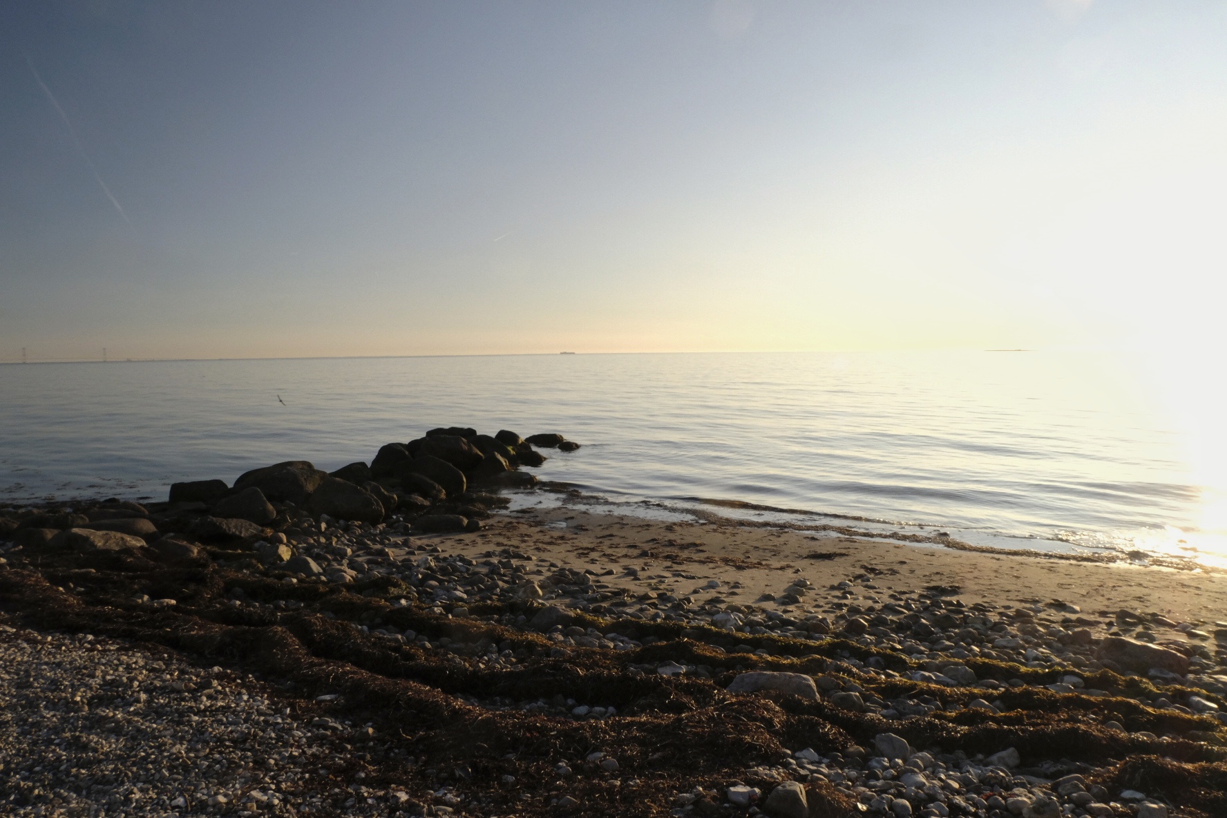 Steiniger Strand mit Felsen im Wasser bei Sonnenaufgang, ruhige See unter klarem Himmel.