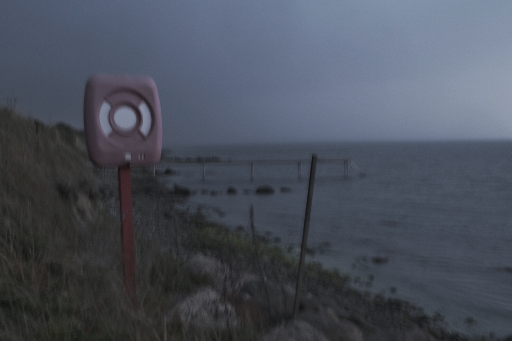 Rote Boje mit Zielkreis an Küste, Meer im Hintergrund, Dämmerung.