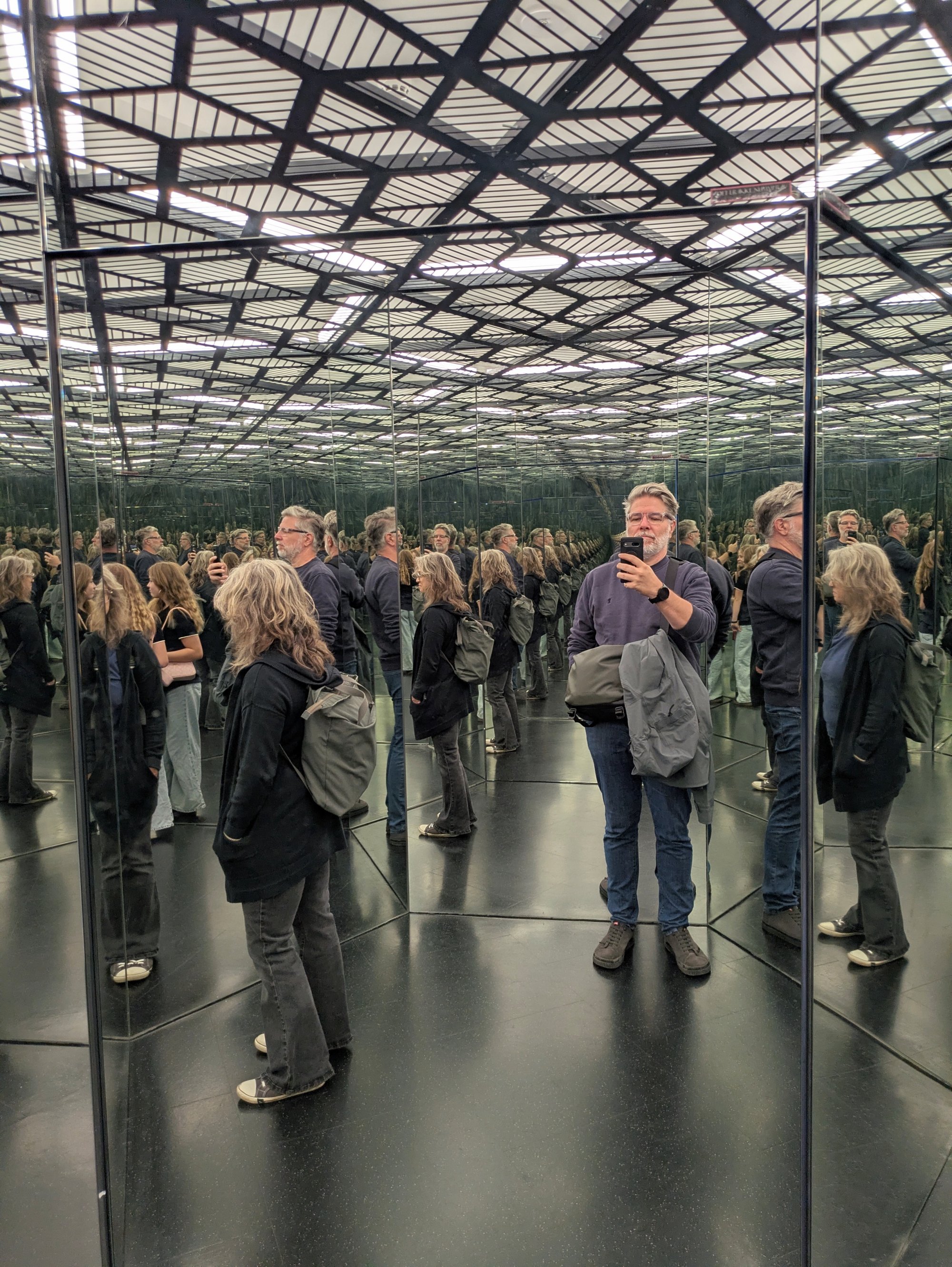 Eine Gruppe von Menschen steht in einem modernen Gewächshaus mit Spiegelwänden. Ein Mann spricht mit Mikrofon zu der Gruppe.