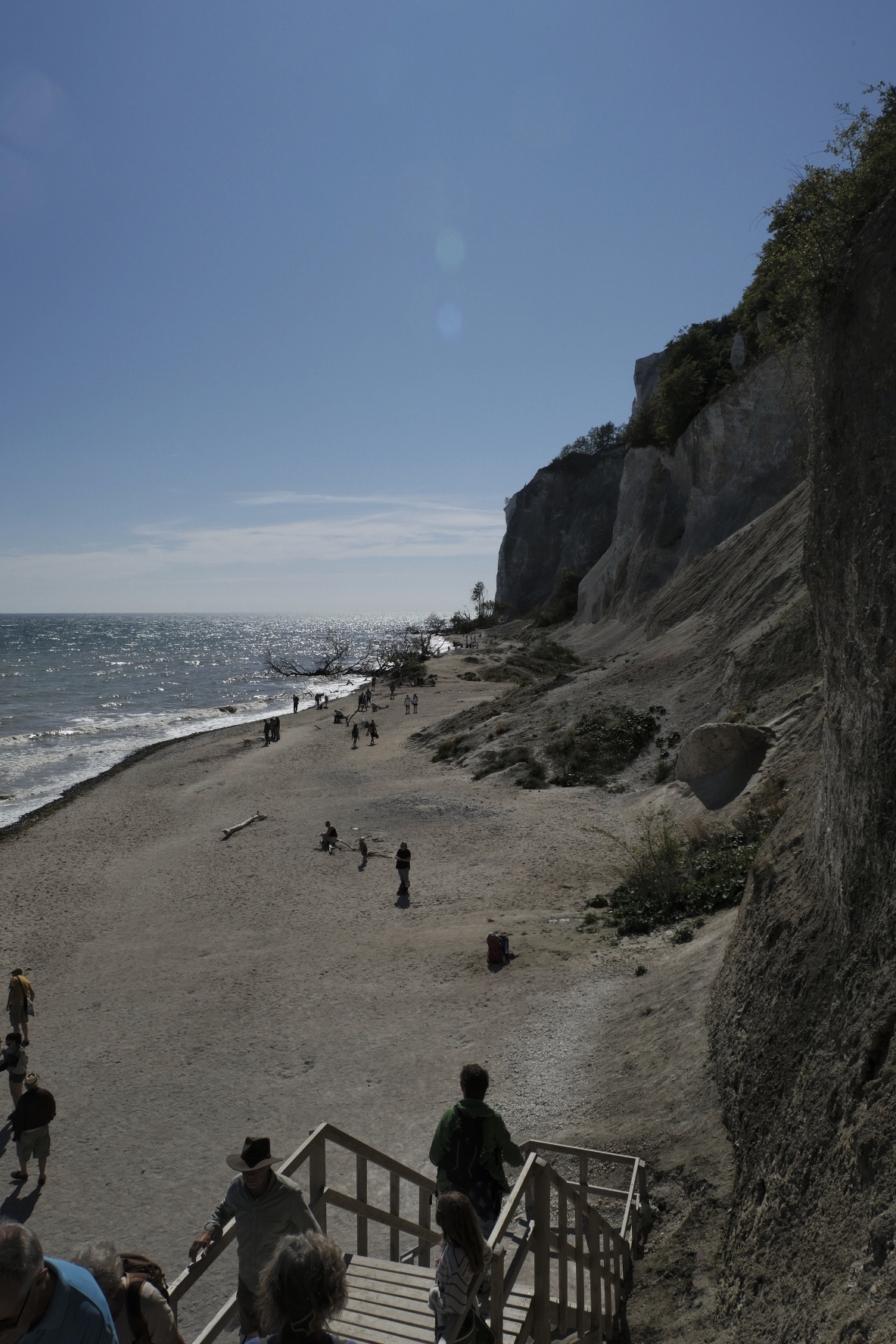 Steilküste mit Strand, Treppen und Besuchern an der Ostsee unter blauem Himmel.