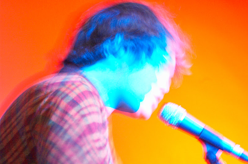 Person mit Mikrofon vor farbigem Hintergrund, Neon-Effekt in Blau, Pink und Orange.