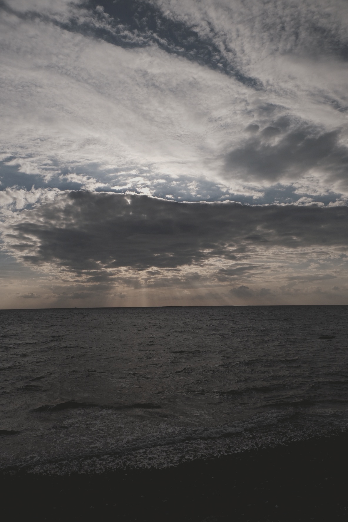 Stürmischer Himmel über ruhigem Meer mit dramatischen Wolkenformationen und Sonnenstrahlen.
