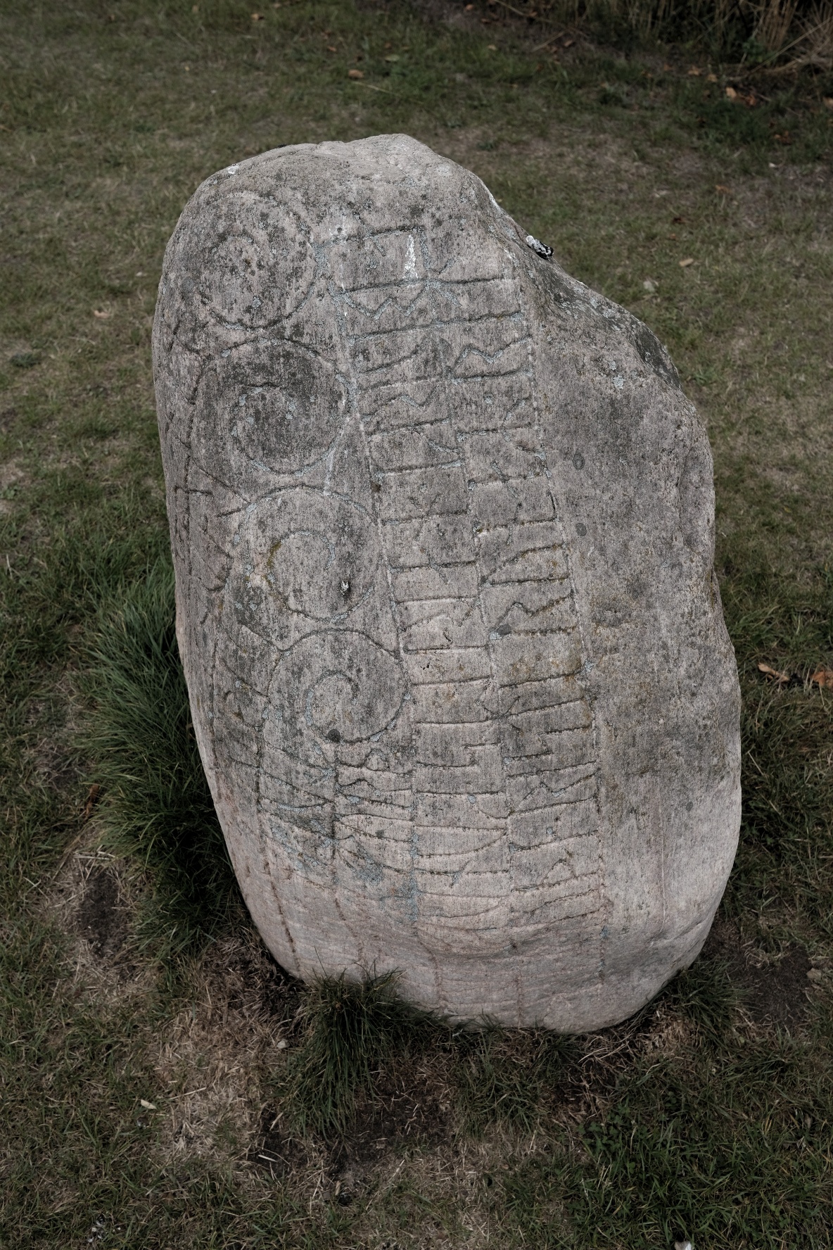 Grauer Stein mit eingeritzten Symbolen und Mustern, im Gras stehend.