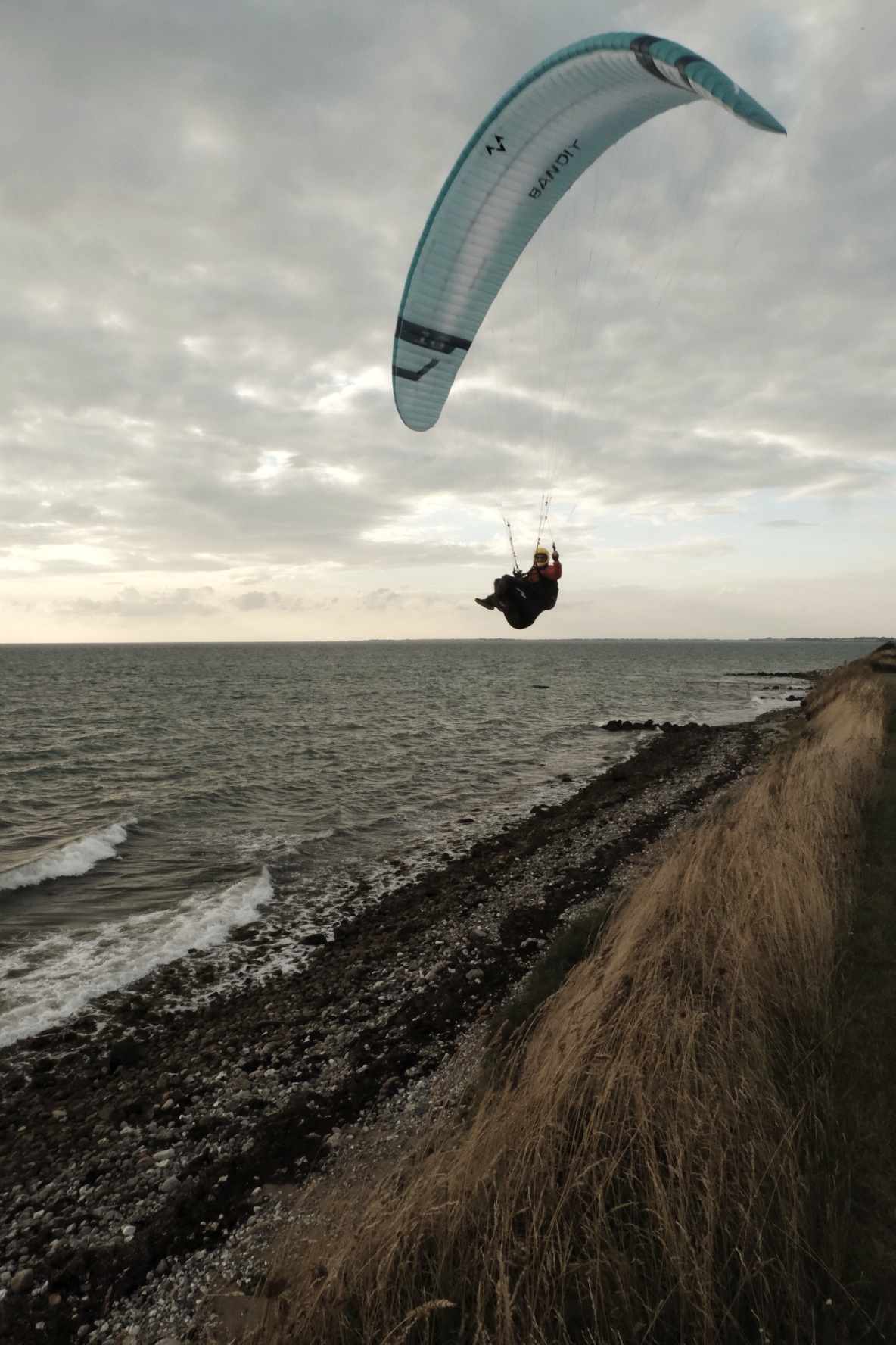 Kitesurfer mit blauem Drachen über der Nordsee, Klippe mit Strandhafer im Vordergrund.