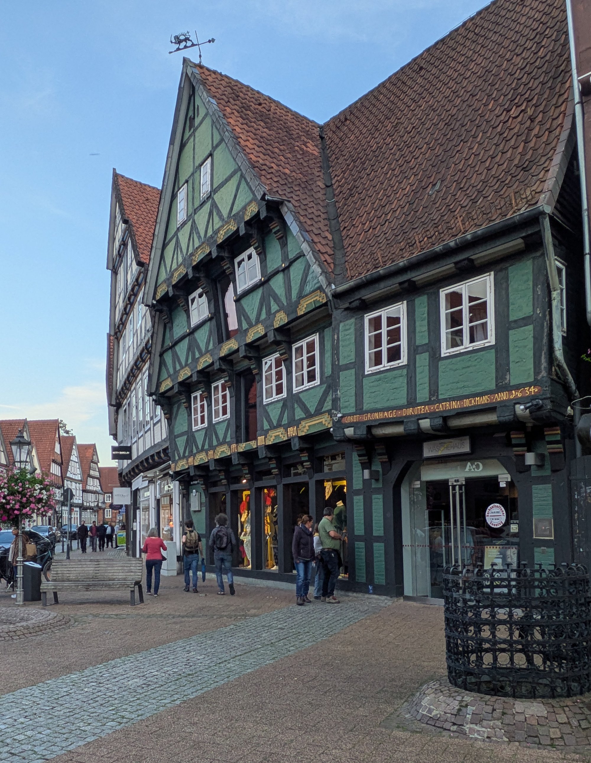 Historisches Fachwerkhaus mit grüner Fassade und roten Ziegeldächern in einer Altstadt, Fußgänger auf Kopfsteinpflaster.