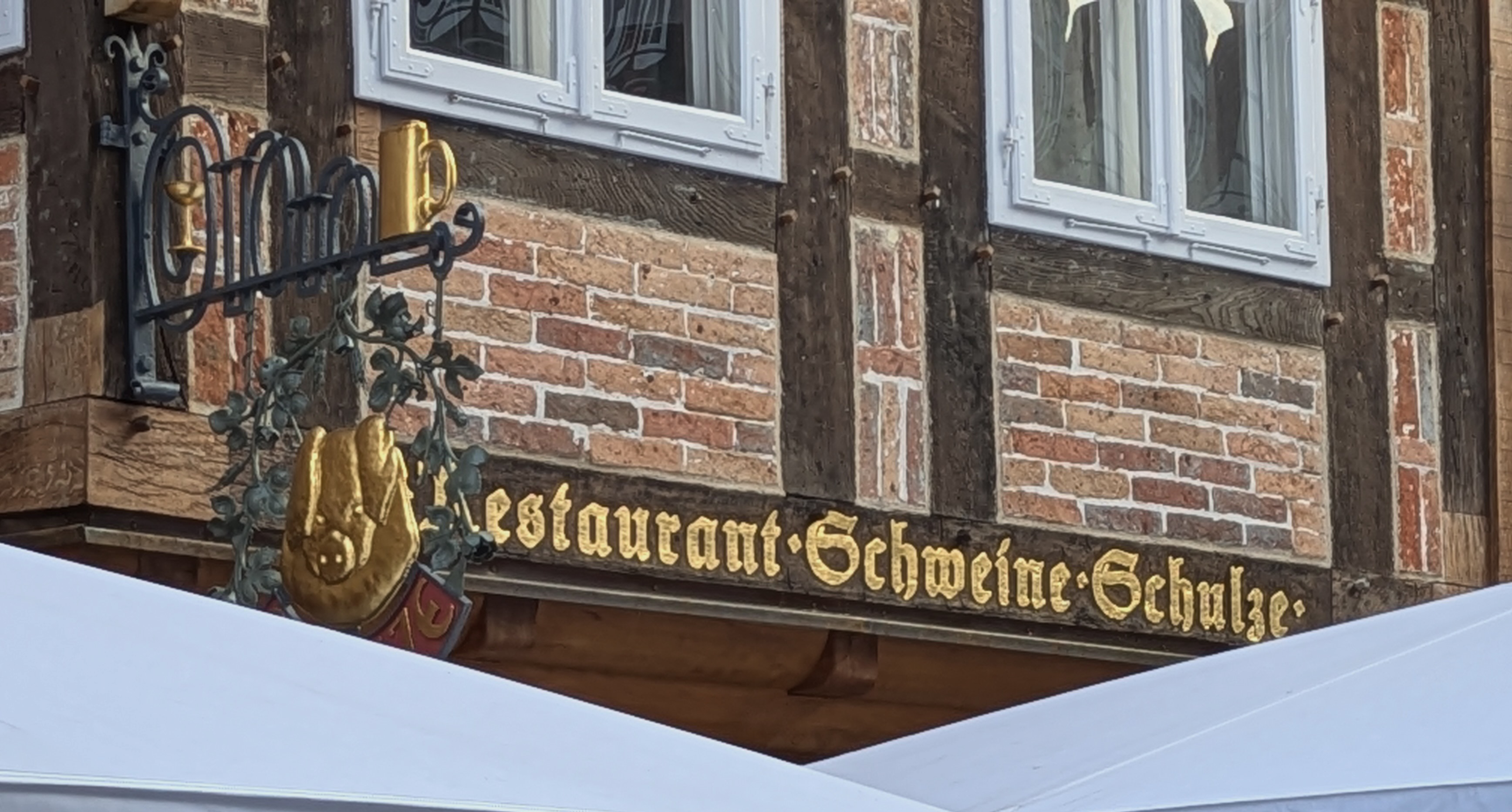 Historisches Restaurant-Schild "Schweine Schulze" an Backsteingebäude mit weißen Fenstern und Schmiedeeisen-Dekoration.